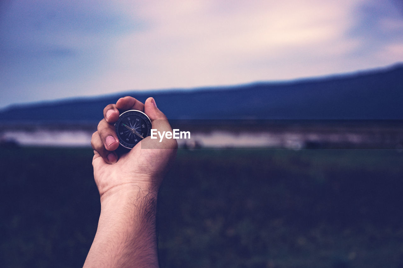 CLOSE-UP OF HAND HOLDING SUNGLASSES AGAINST SKY