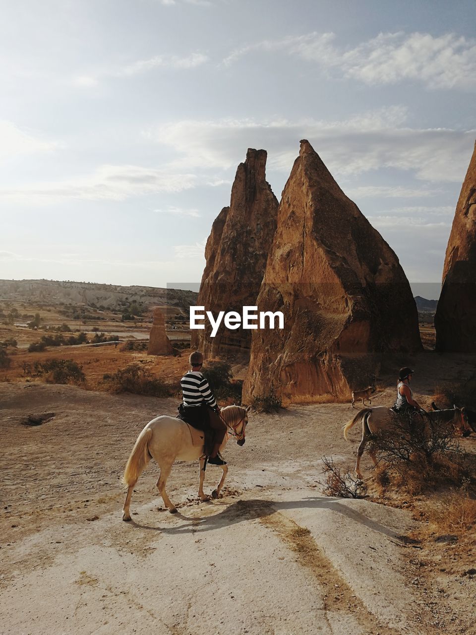 People riding horses on dirt road against rock formations