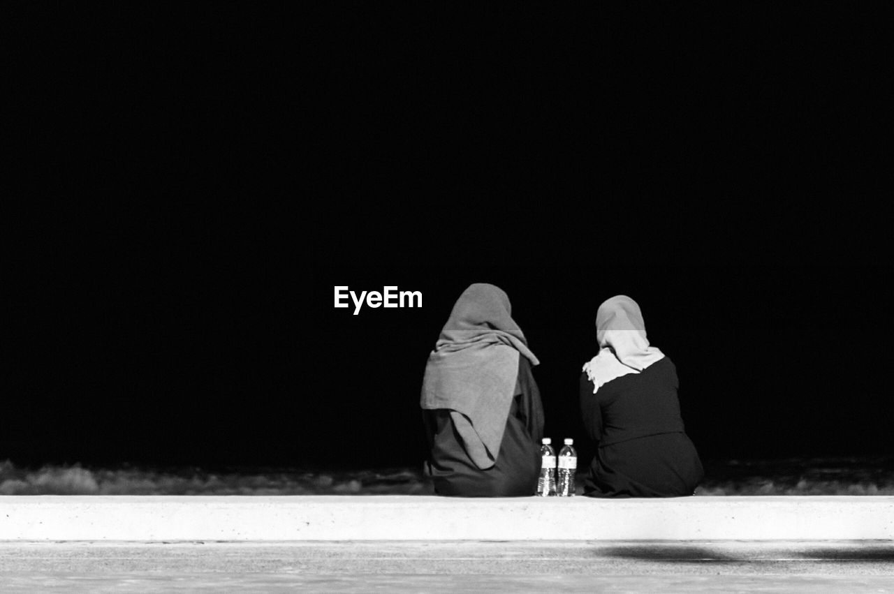 Rear view of female friends on beach against clear sky at night