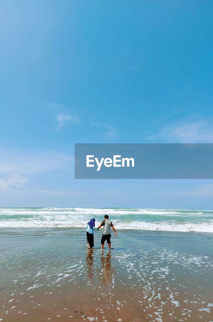 Rear view of men on beach against sky