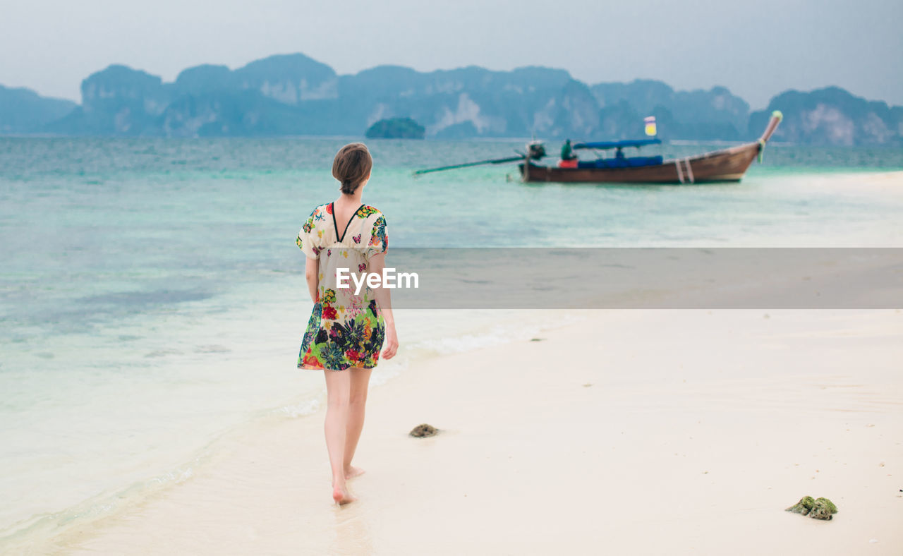 Woman walking on sea shore by moored longtail boat at beach