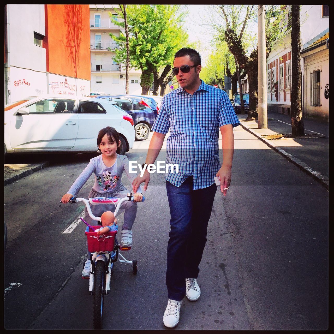 Portrait of girl riding bicycle with father walking on street