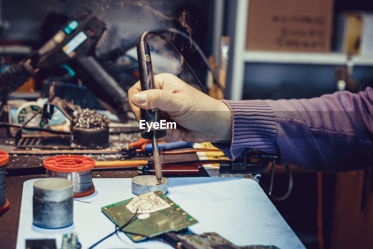 Cropped image of person repairing circuit board on table indoors