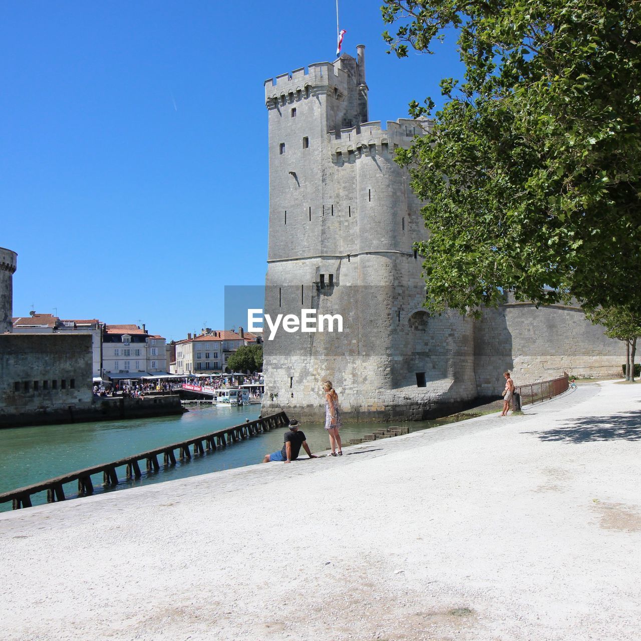 People by historic tower at harbor against sky