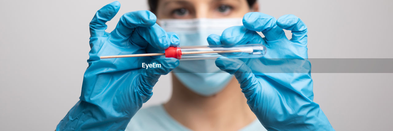 Close-up of doctor wearing mask holding test tube against gray background