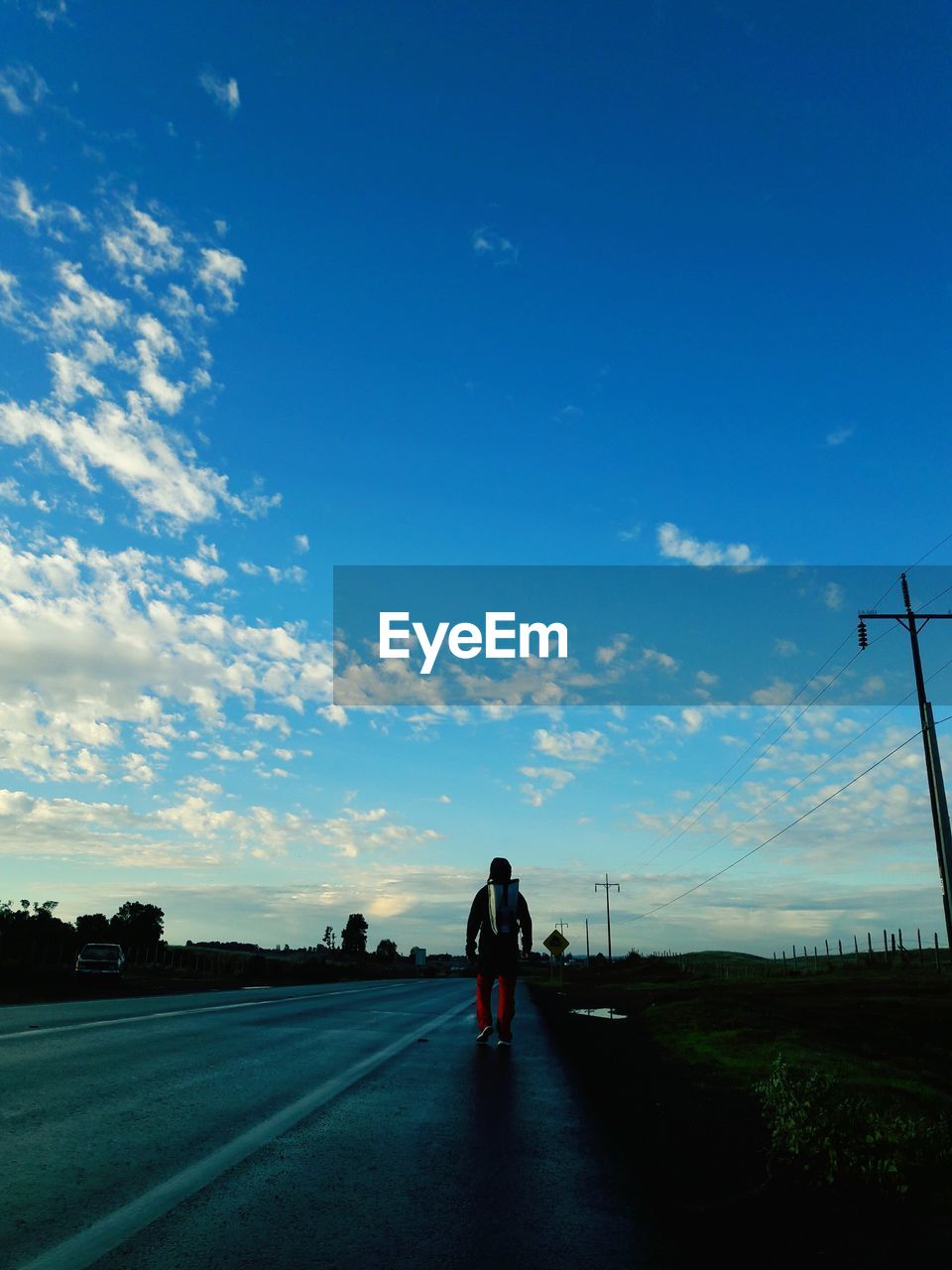 Rear view of man walking on road against blue sky