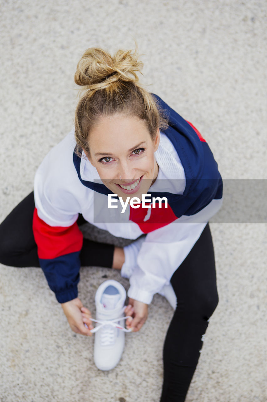 High angle portrait of smiling young woman sitting on footpath