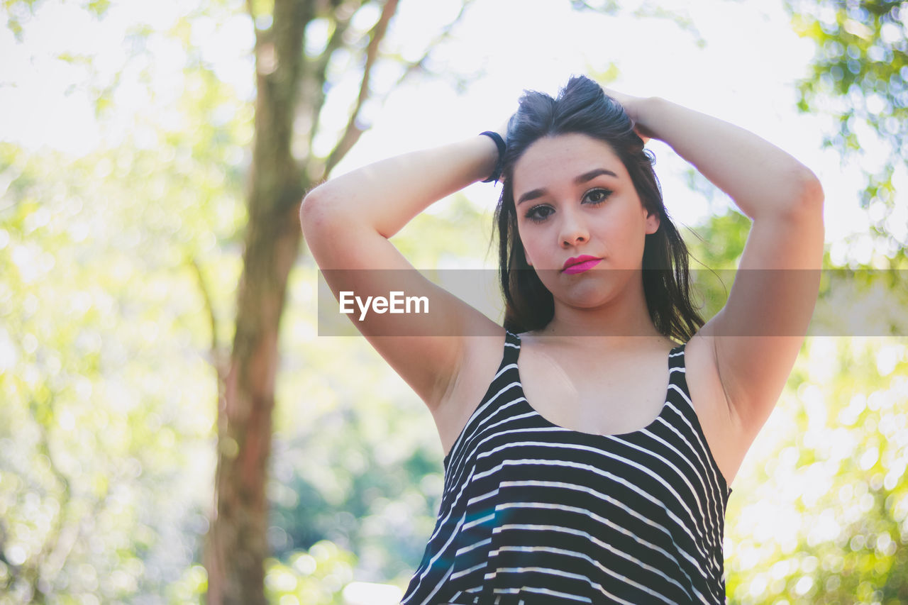 Portrait of beautiful woman standing against trees