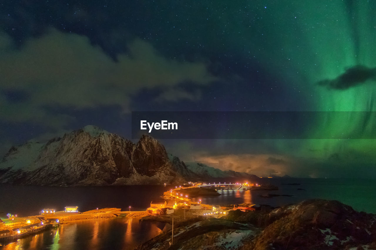 Illuminated city by sea against sky at night