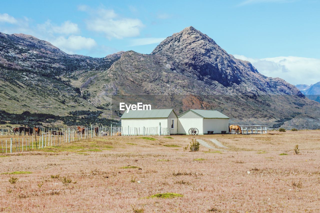 BUILT STRUCTURE ON FIELD BY BUILDINGS AGAINST MOUNTAINS