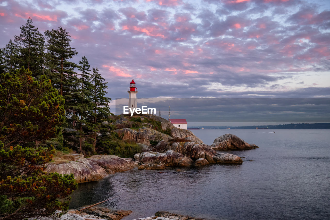 LIGHTHOUSE AMIDST ROCKS BY SEA AGAINST SKY