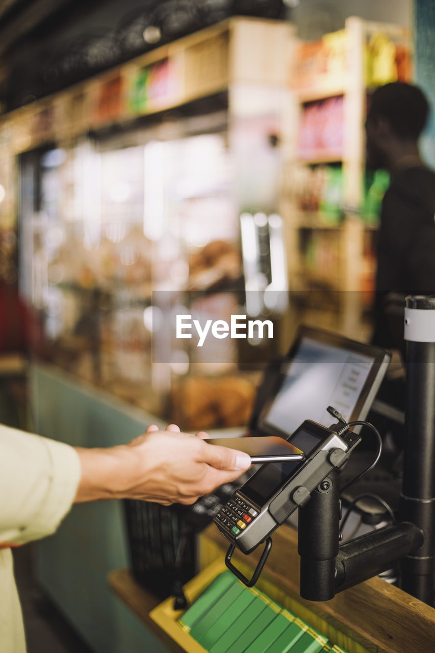 Hand of young male customer paying through smart phone at store checkout