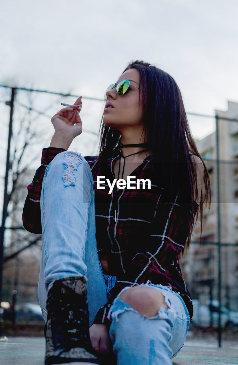 Low angle view of woman smoking while sitting against sky