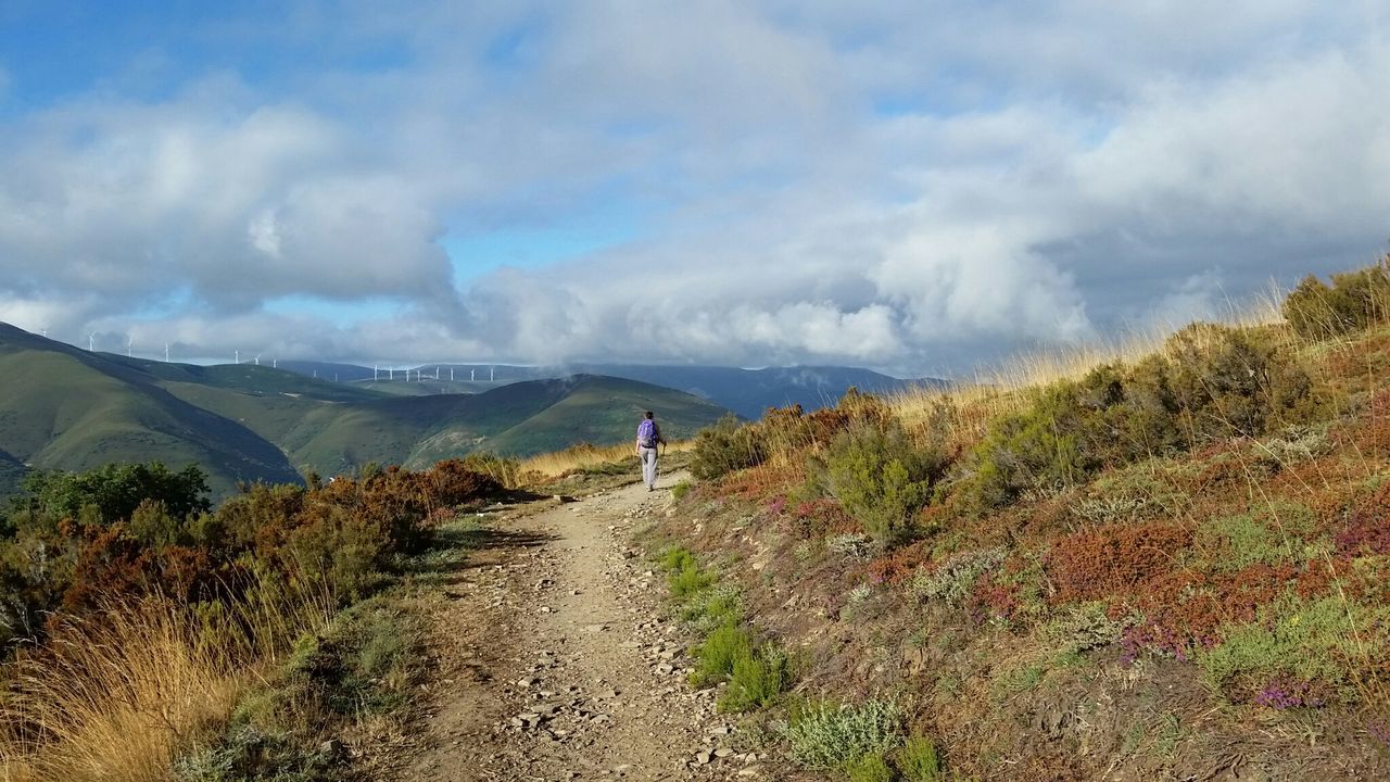 Rear view of hiker on dirt trail at mountain against sky