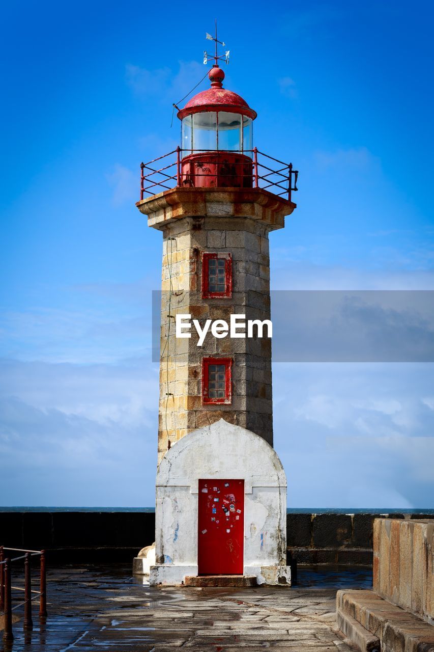 Lighthouse by building against sky