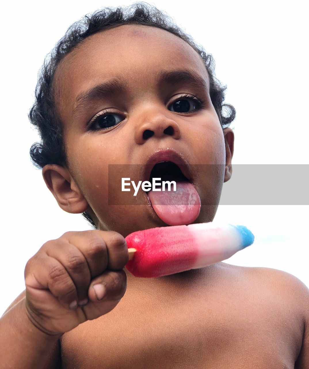 Close-up portrait of shirtless boy eating popsicle against clear sky