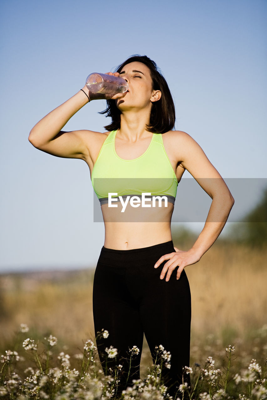 Woman drinking water while standing against clear sky