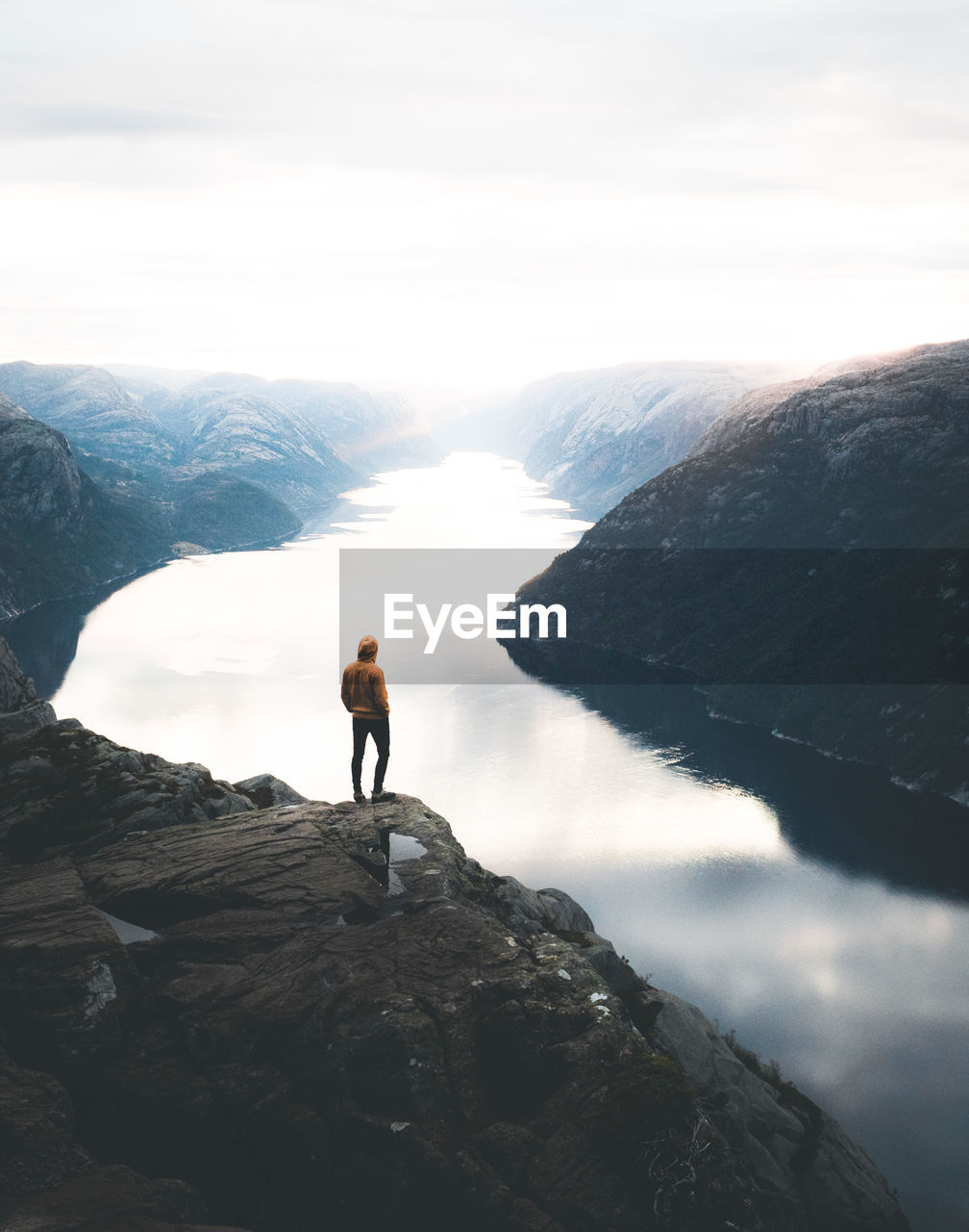 Rear view of man standing by cliff against lake