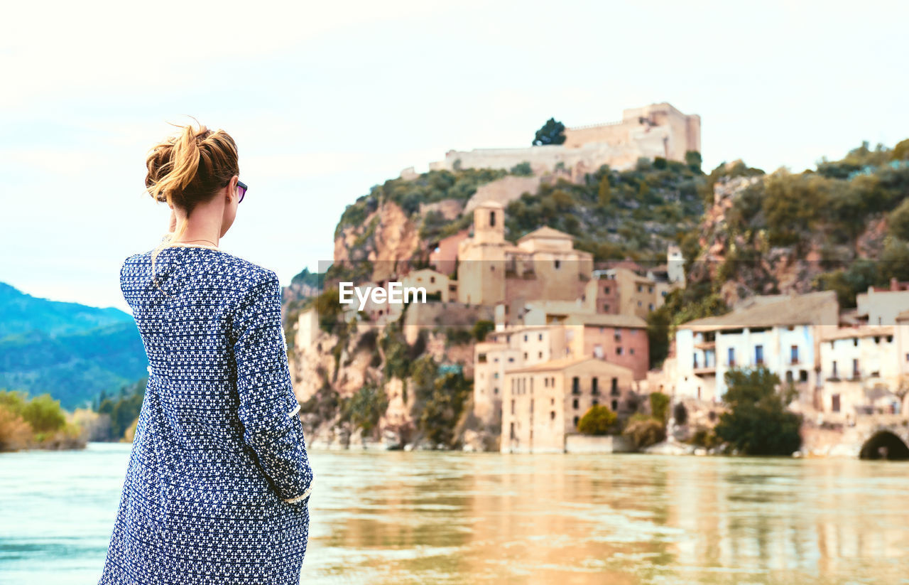 Rear view of woman standing by ebro river against miravet village