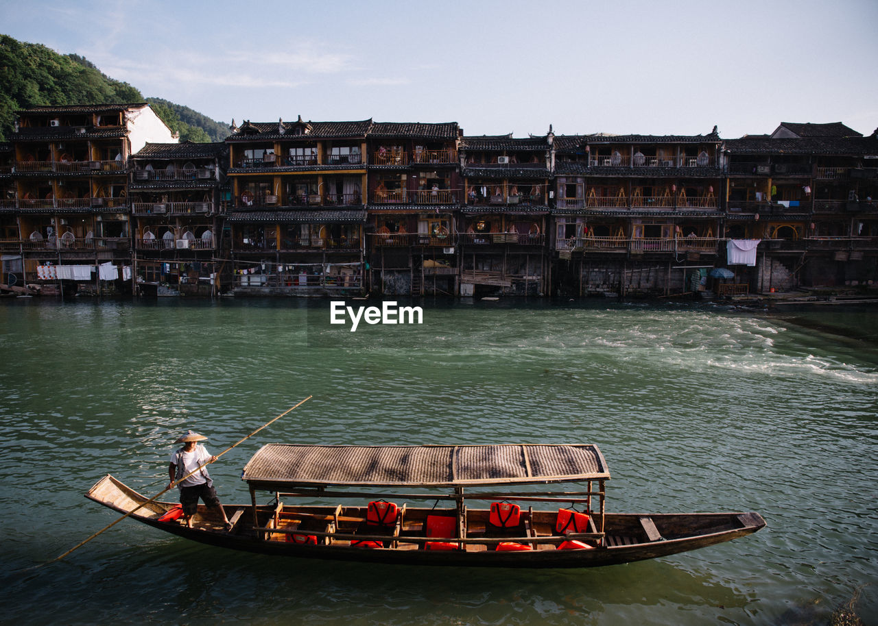 Man on gondola in canal against buildings during sunny day