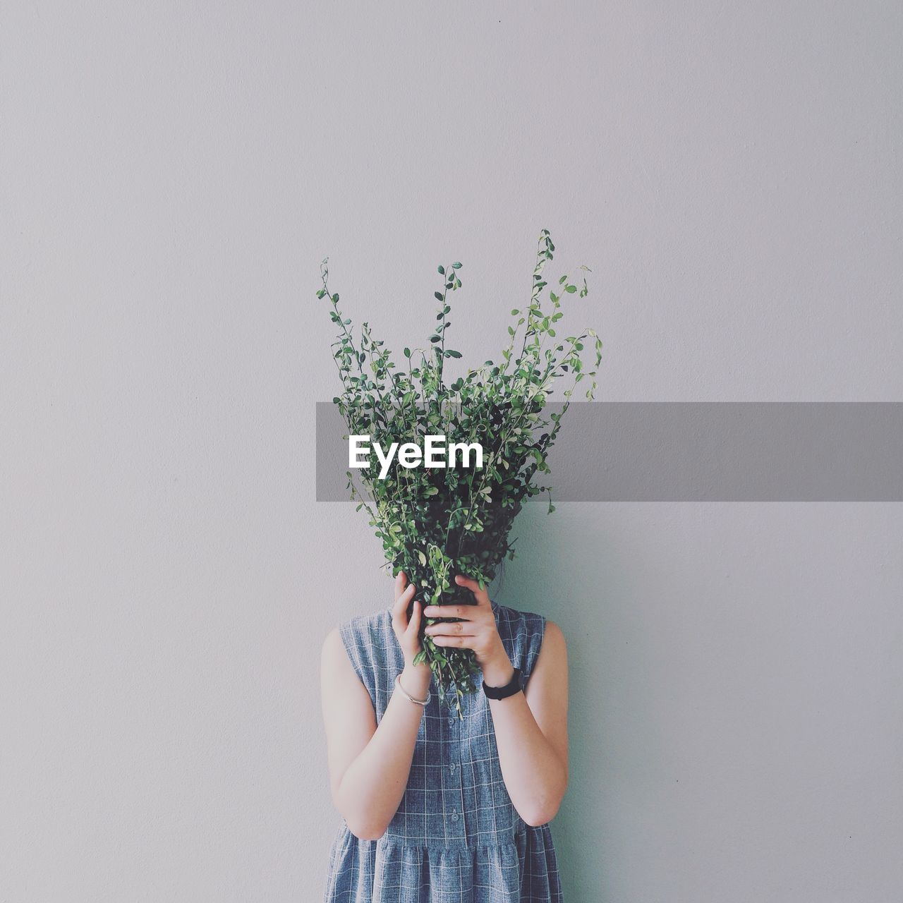 Woman covering face with plants against wall