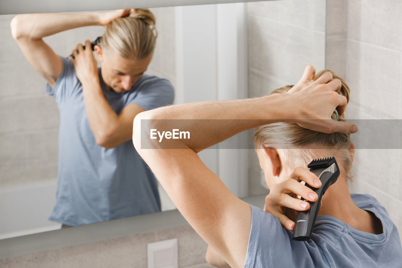 Personal hygiene, caucasian man cutting his own hair in the bathroom with wireless electric shaver
