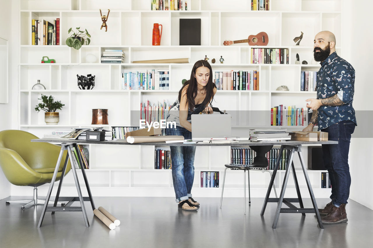 Architects working at table against bookshelf in home office