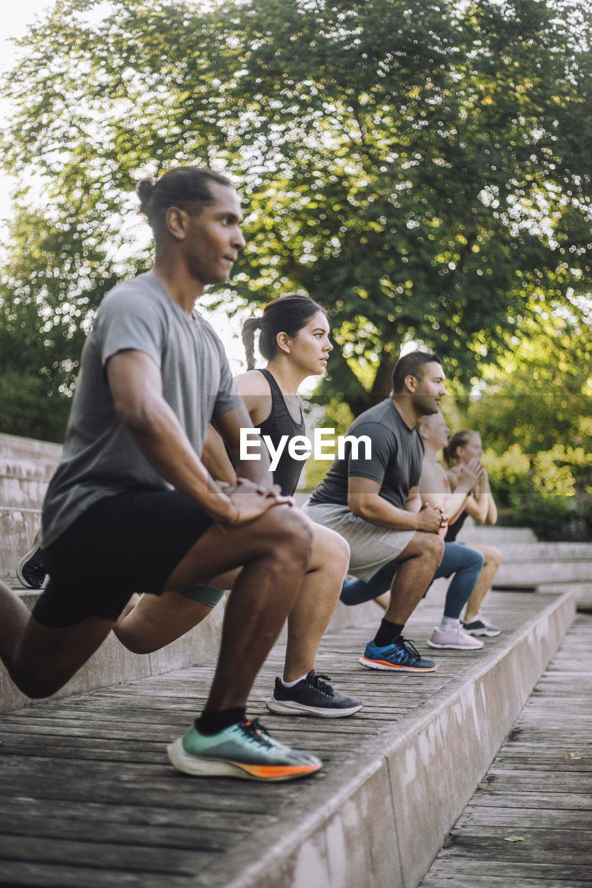 Focused male and female friends practicing lunges on steps