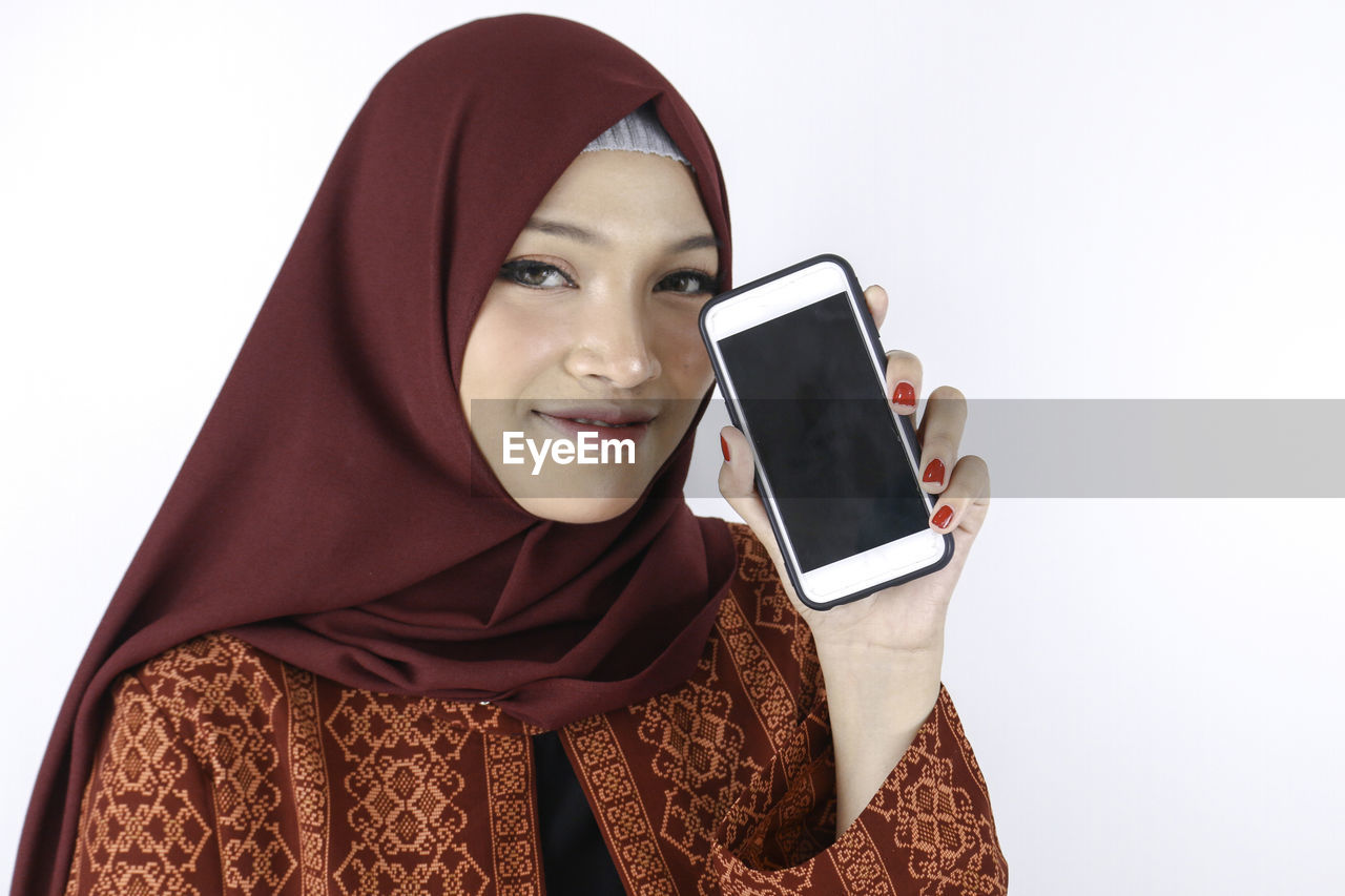 PORTRAIT OF SMILING YOUNG WOMAN USING SMART PHONE