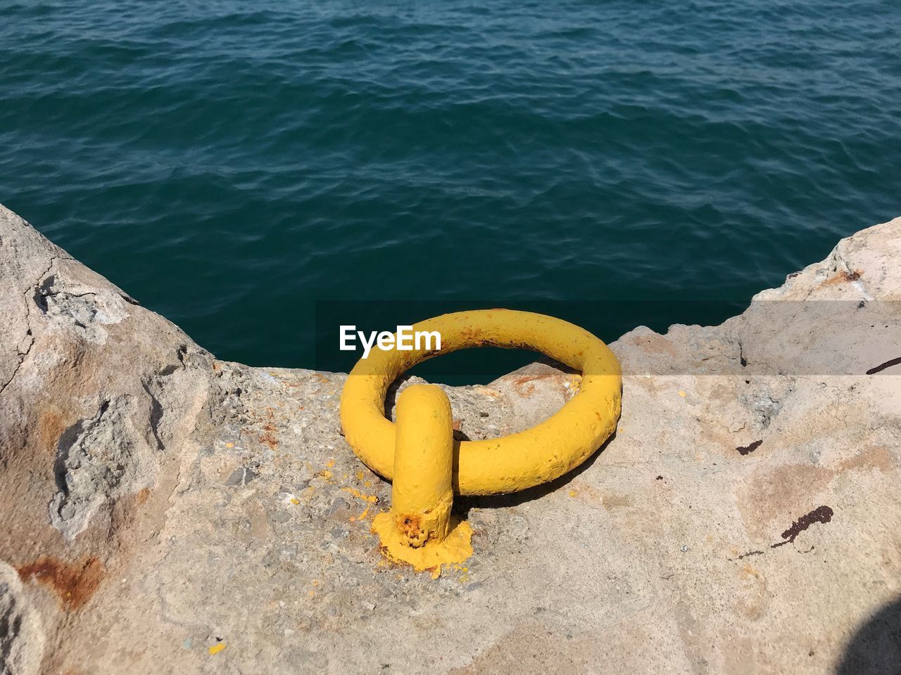 High angle view of yellow painted iron ring on quay wall