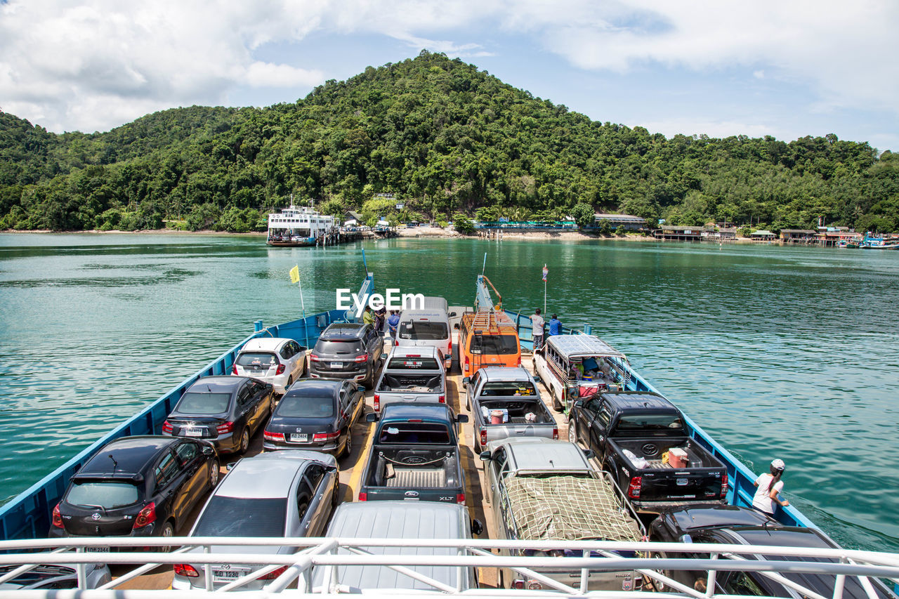 Cars on ferry at river against mountain