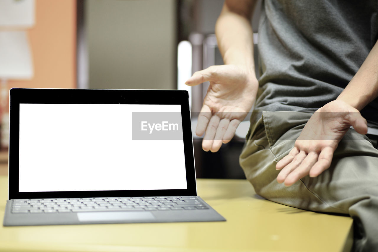 Midsection of man showing laptop on table in office