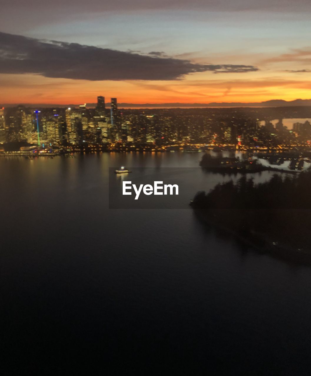 High angle view of illuminated buildings by river against sky during sunset