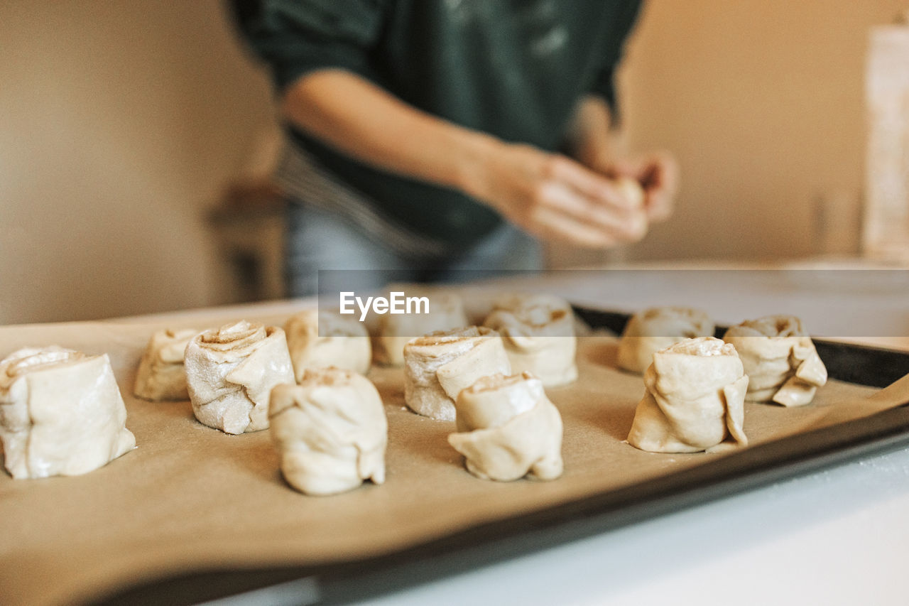 Arranged cinnamon rolls on baking sheet while woman in background at kitchen