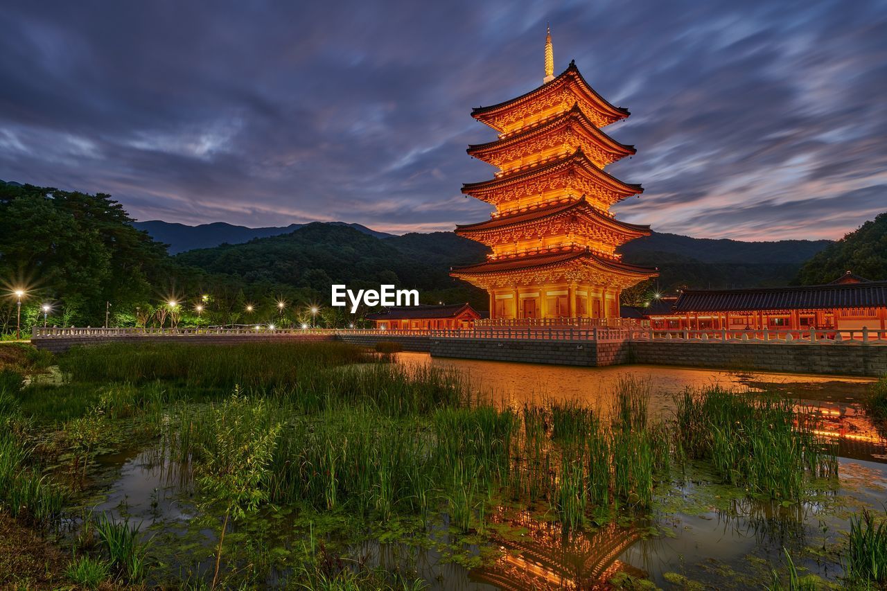 ILLUMINATED BUILDING BY LAKE AGAINST SKY AT NIGHT