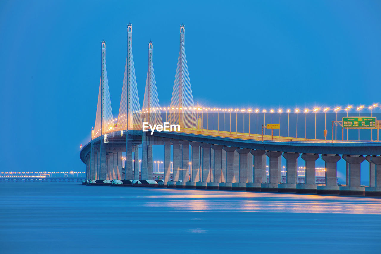 Illuminated bridge over sea against sky at dusk