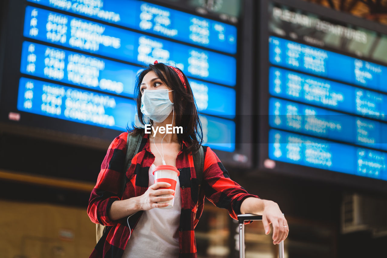 Young woman wearing mask looking away while standing at airport