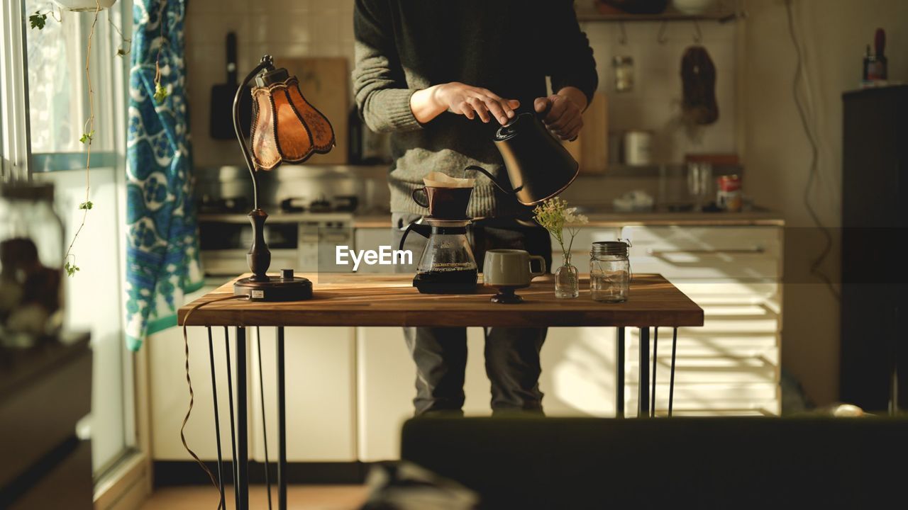 Midsection of man using mobile phone at table and making coffes