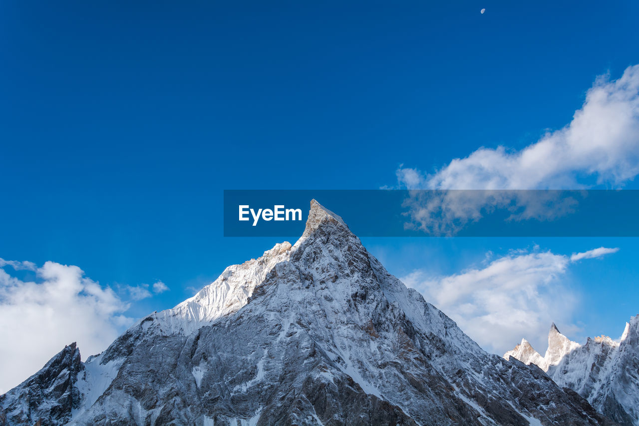 Low angle view of snowcapped mountains against blue sky