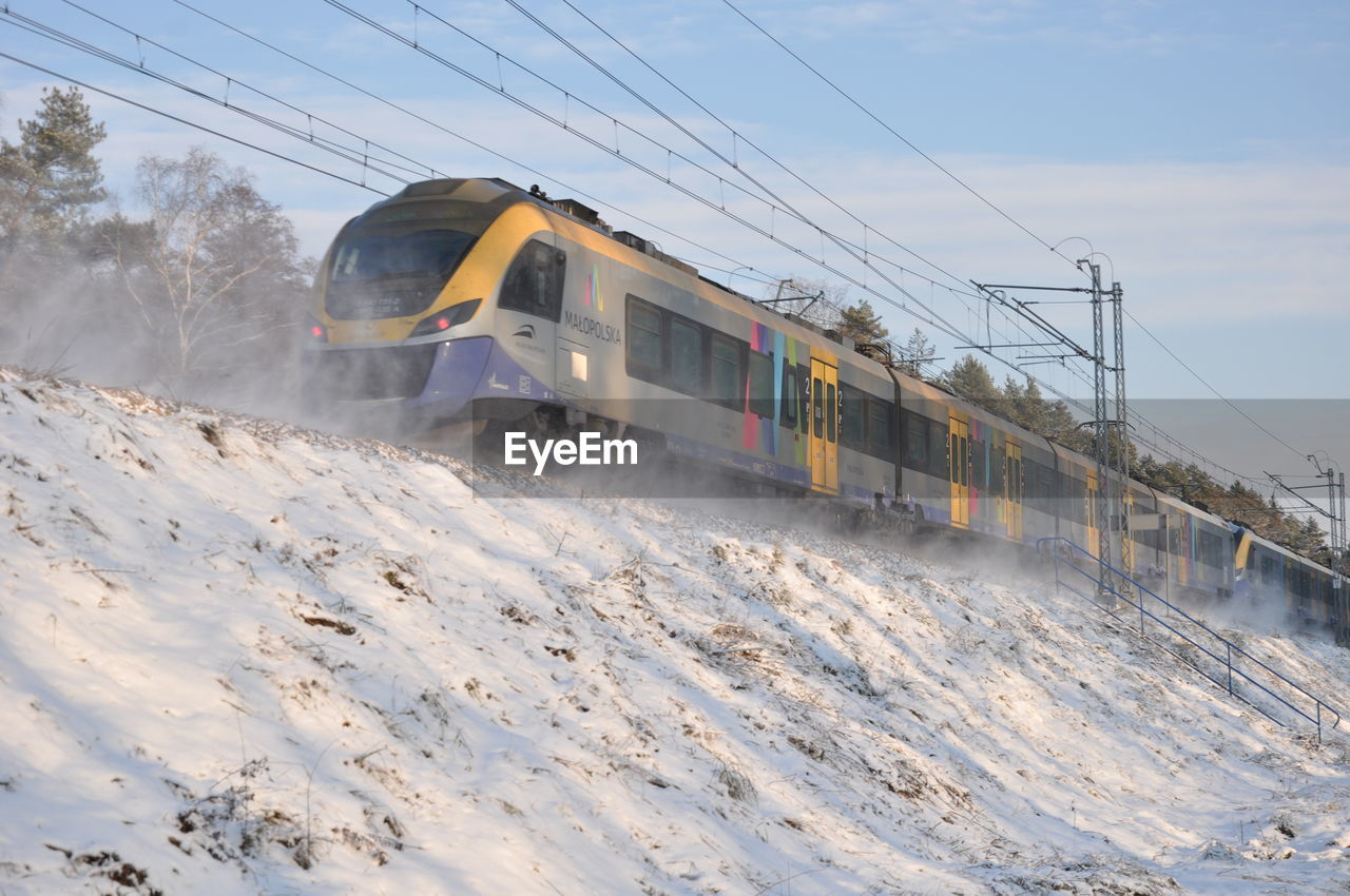 TRAIN ON SNOW COVERED RAILROAD TRACKS AGAINST SKY