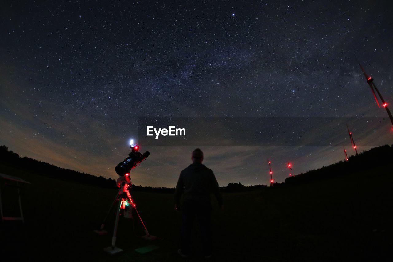 Rear view of man standing by camera against sky at night