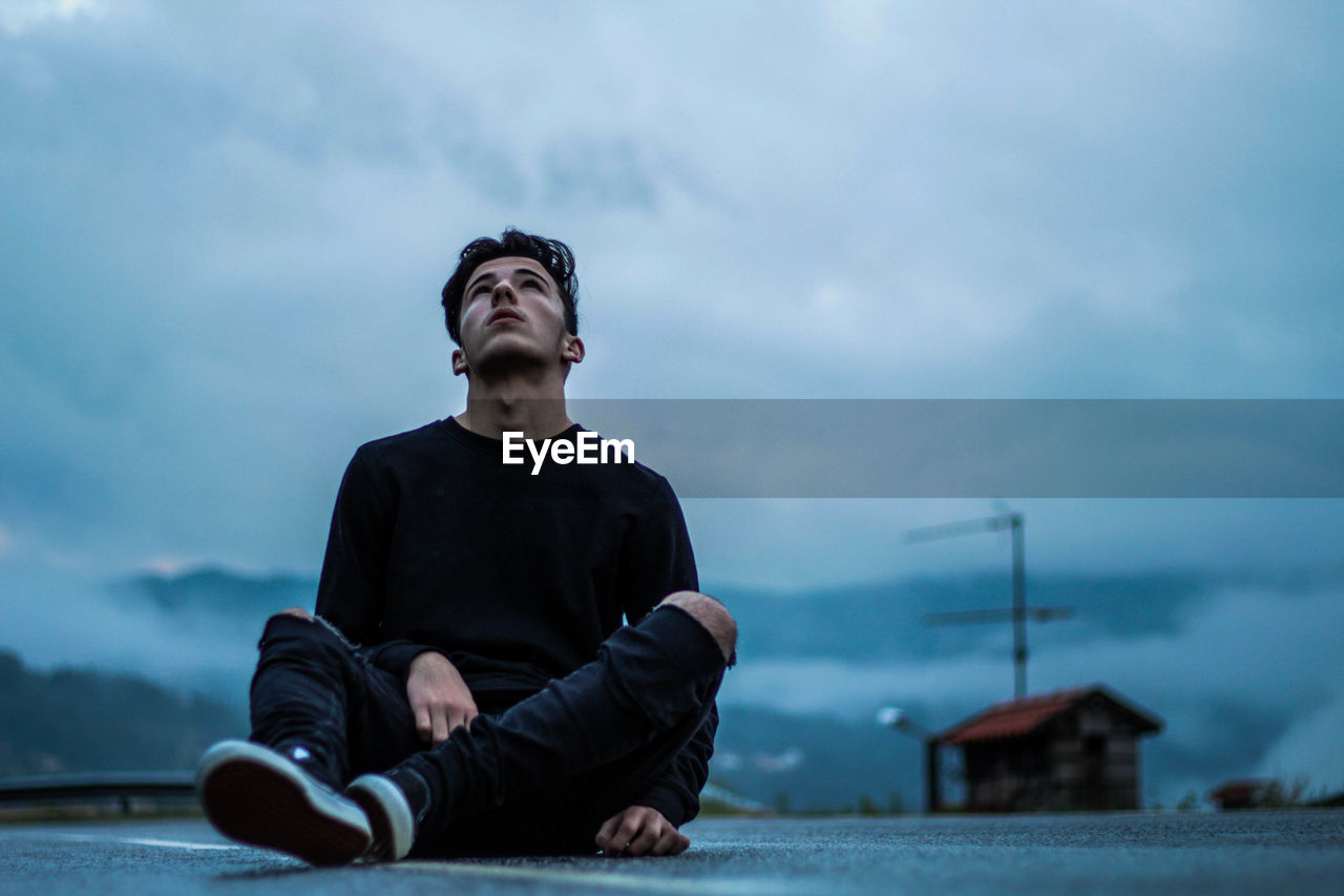 Young man sitting against sky