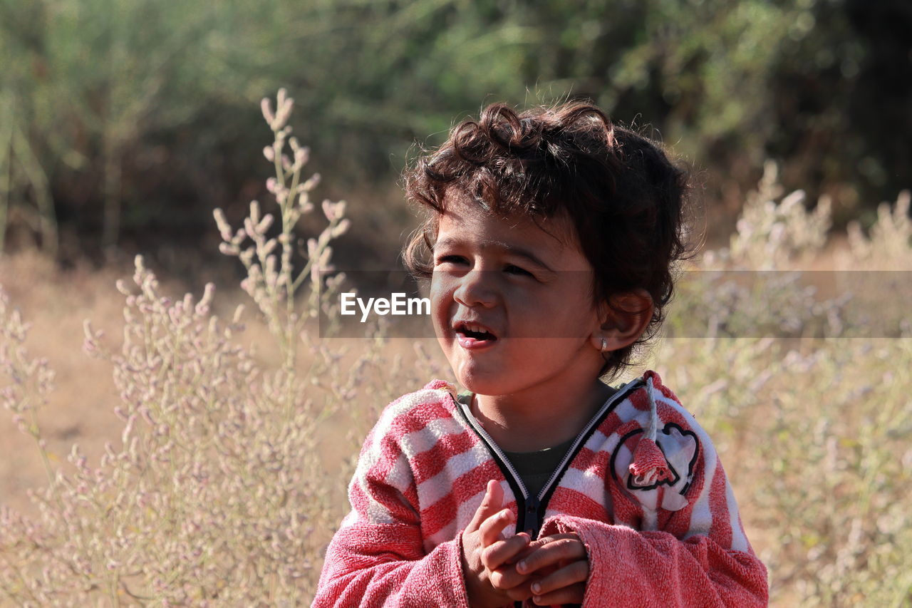 A beautiful little indian child stands in the field and the natural blur background of white bushes