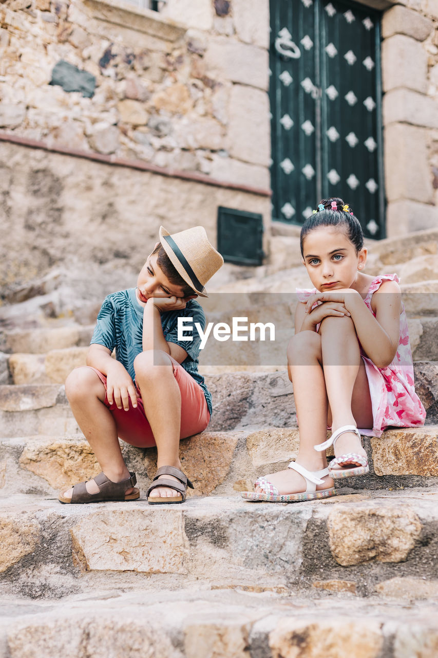 Sad siblings sitting on staircase in city