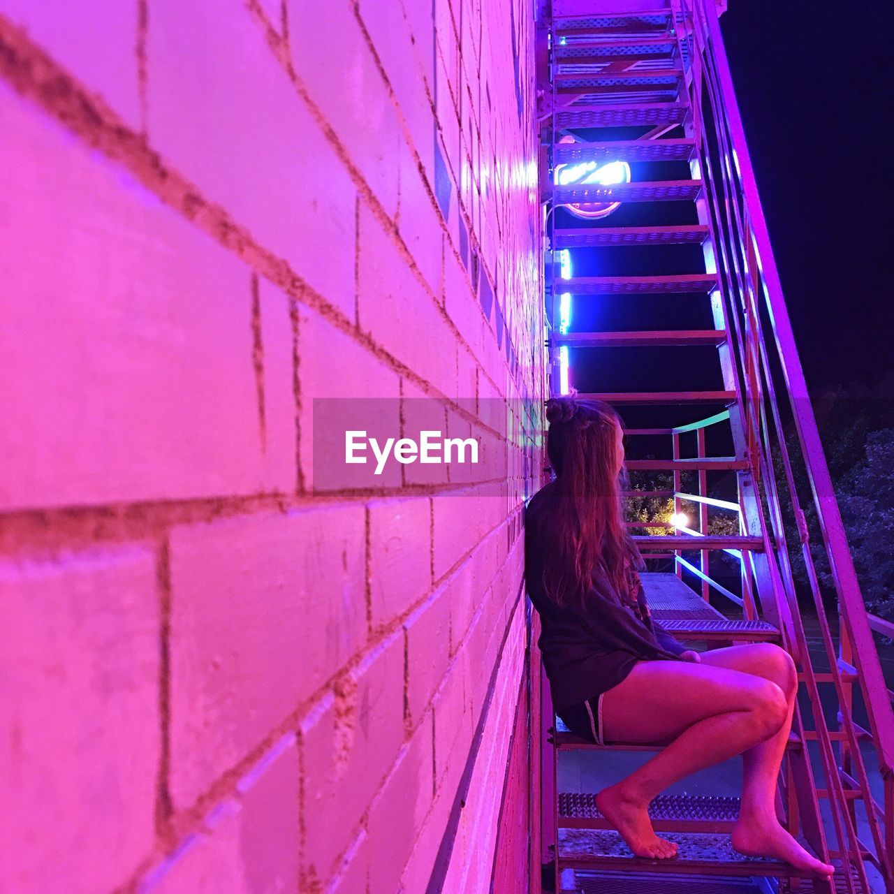 SIDE VIEW OF YOUNG WOMAN SITTING ON ILLUMINATED WALKWAY