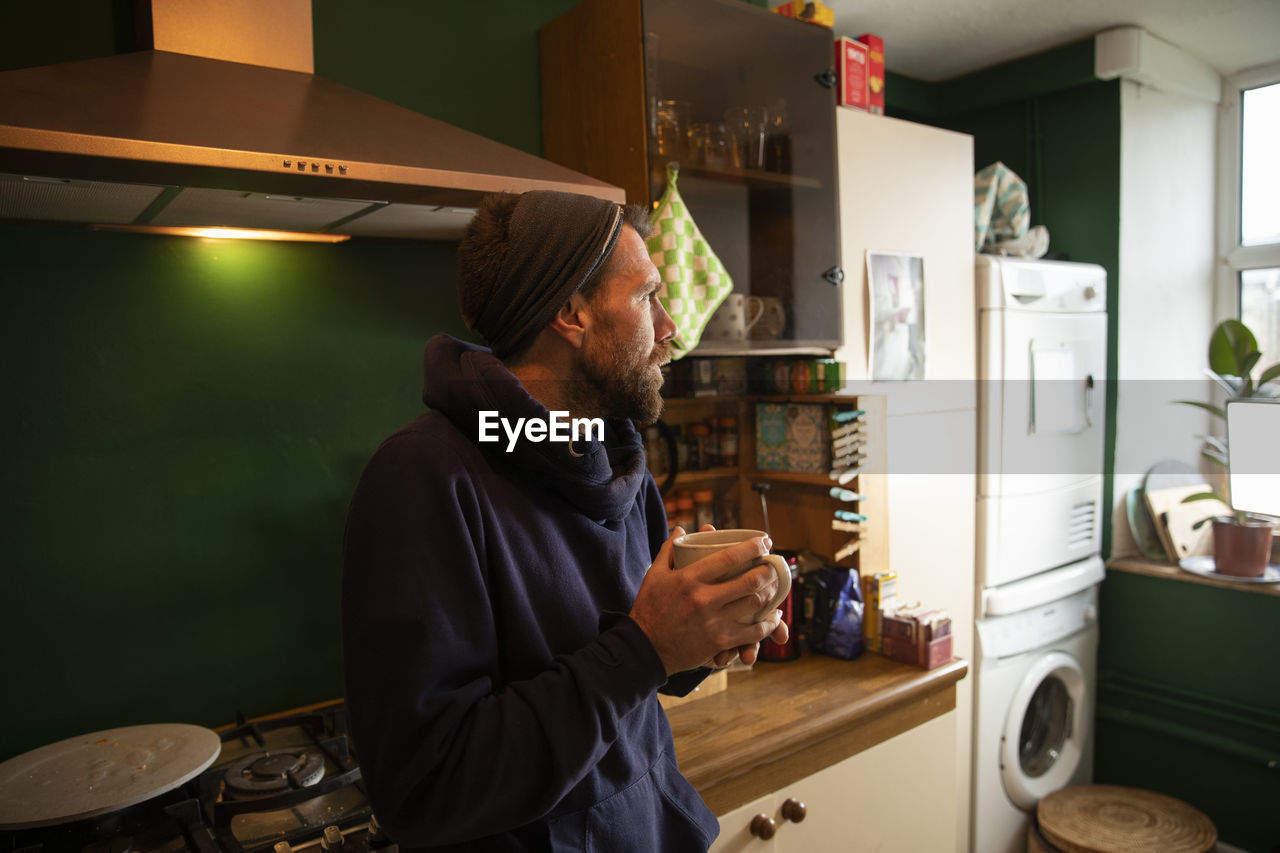 Thoughtful man holding cup in kitchen at home