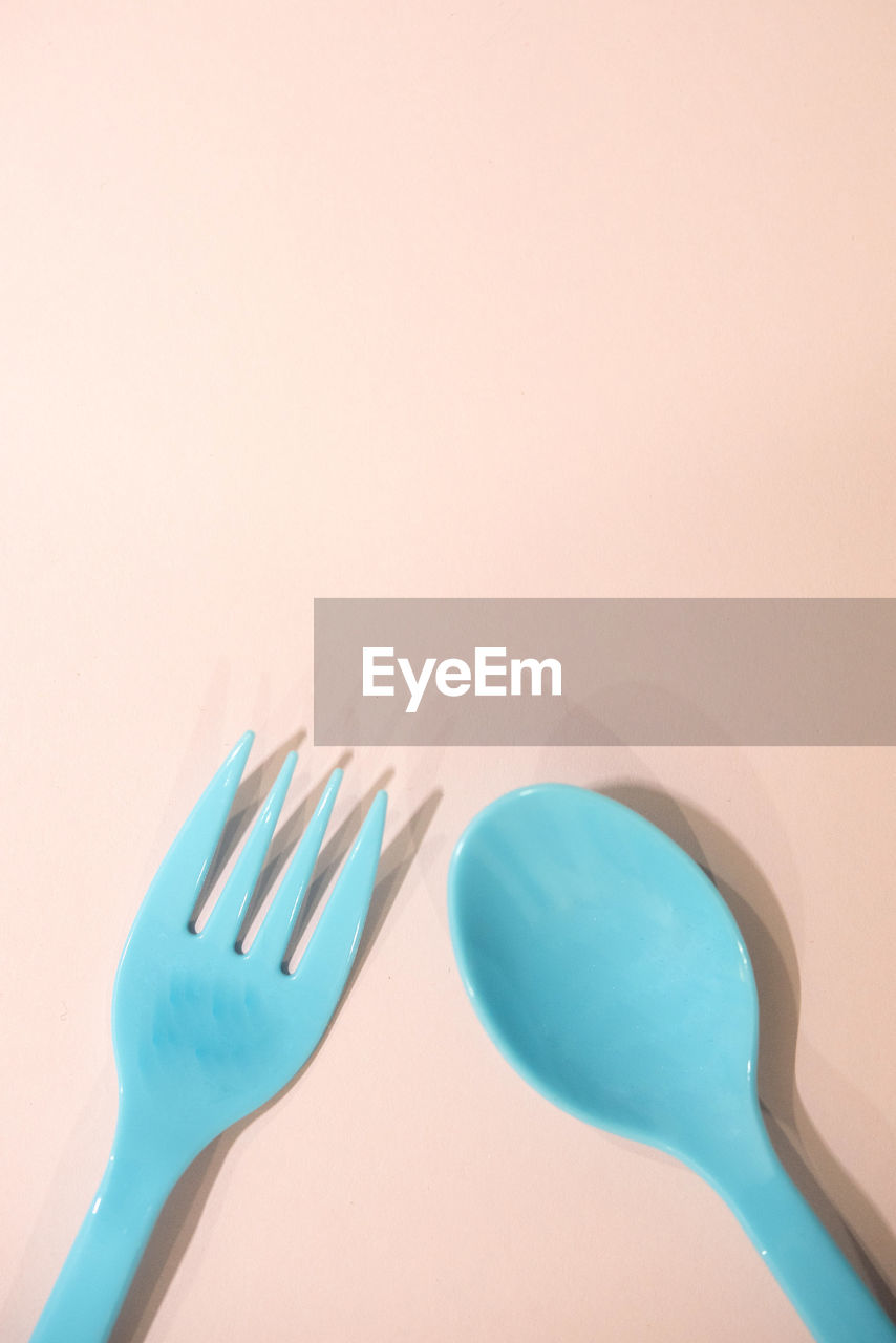 Close-up of blue plastic cutlery over peach background