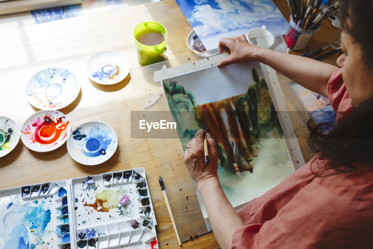 Woman with paintbrush doing watercolor painting at home