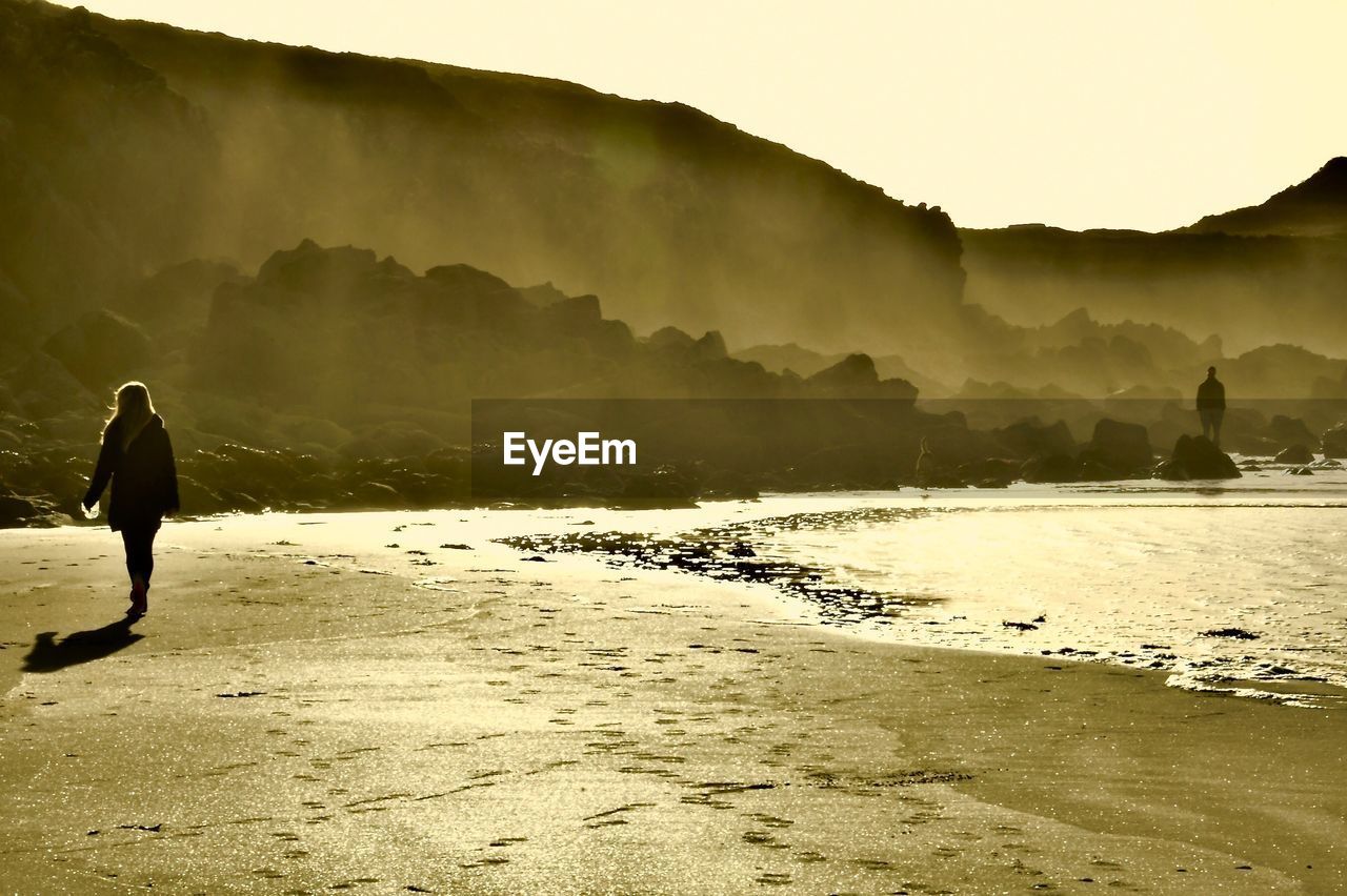 REAR VIEW OF MAN ON SHORE AT BEACH AGAINST SKY