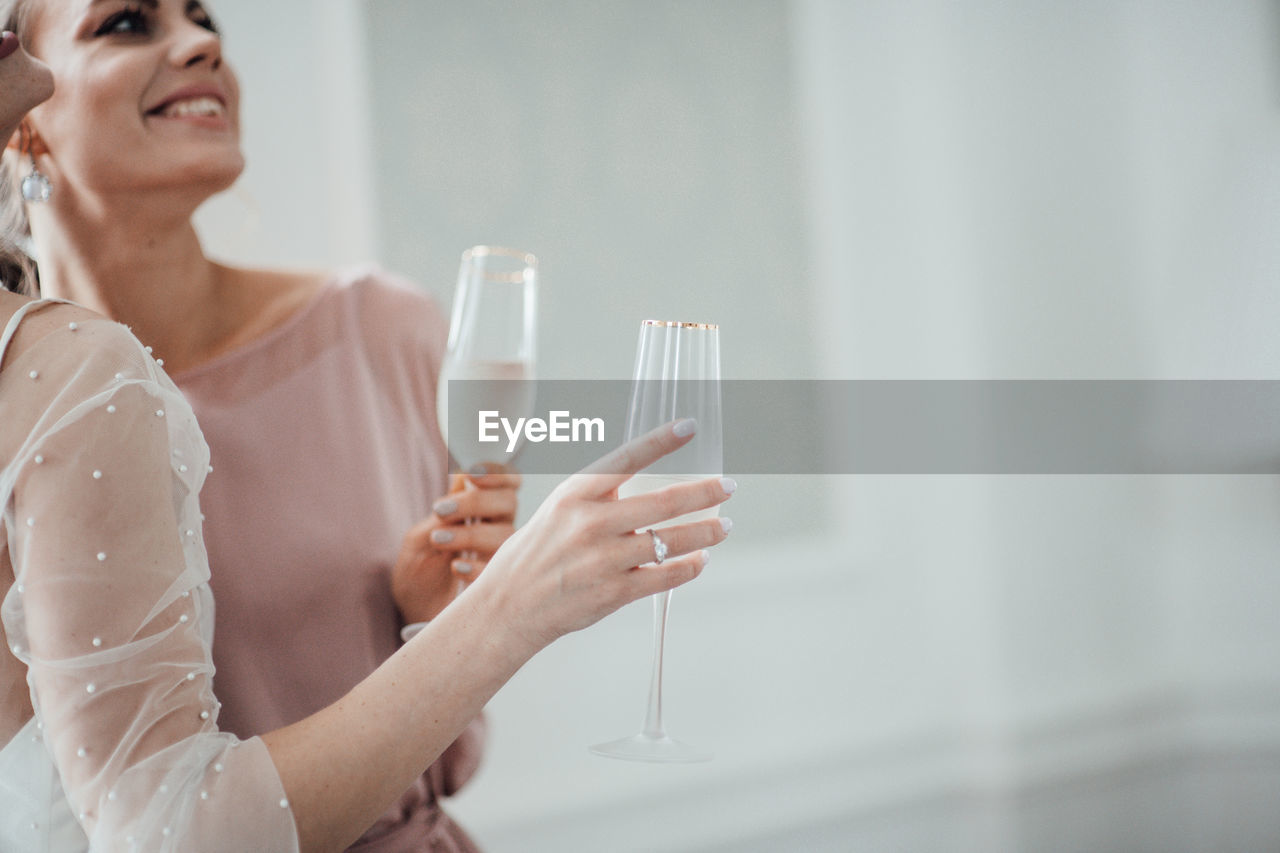 Midsection of bridesmaid and bride holding champagne flute